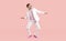 Cheerful cool young man in suit shows funny dance moves isolated on pink background.