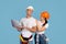 Cheerful couple in hardhats posing with laptop computer on blue studio background