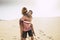 Cheerful couple in love with man carry on the young beautiful woman on his back walking on the sandy desert under a sunny day of