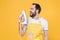 Cheerful crazy young man househusband in casual white t-shirt apron doing housework isolated on yellow wall background