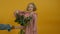 Cheerful curly kid looking at flowers and jumping on yellow background