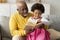 Cheerful cute african american little granddaughter and senior grandpa reading book with fairy tales on sofa
