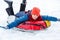 Cheerful cute young boy in orange hat red scarf and blue jacket holds tube on snow, has fun, smiles.