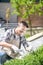 Cheerful dark-haired male in protective glasses and gloves pruning bushes outside, smiling, crouching