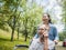 Cheerful disabled senior man talking on smartphone while granddaughter pushing a wheelchair in the park. Family life on vacation