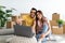 Cheerful diverse couple with laptop searching for household goods for their new home online, using pc on moving day