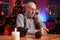 Cheerful elder man using a mobile phone sitting at table in room