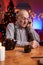 Cheerful elder man using a mobile phone sitting at table in room