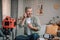 Cheerful elderly european man with beard uses headphones to shooting blog in living room interior