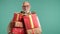 Cheerful elderly man carrying festive gifts, in white shirt on turquoise