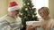 Cheerful elderly married couple celebrating Christmas. Husband wearing a Santa hat gives his wife a gift.