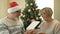 Cheerful elderly married couple celebrating Christmas. Husband wearing a Santa hat gives his wife a gift.