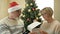 Cheerful elderly married couple celebrating Christmas. Husband wearing a Santa hat gives his wife a gift.