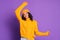 Cheerful ethnic African-American woman in yellow sweater and hat dances and enjoys life on colorful purple background