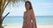 Cheerful ethnic female standing near palm on beach