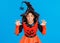 cheerful ethnic girl in pumpkin costume scary gestures and celebrates Halloween and laughs on a bright blue background