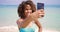 Cheerful ethnic woman taking selfie on beach