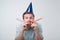 cheerful european young man having fun on party wearing blue denim shirt and holiday hat, blowing party horn