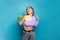 Cheerful excited emotional woman singing with green plastic bottle against blue studio wall background