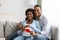 Cheerful expecting couple sitting on couch, holding red heart