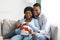 Cheerful expecting couple sitting on couch, holding red heart