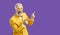 Cheerful extravagant and funny senior man pointing fingers at copy space on purple background.