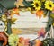 Cheerful fall or autumn border with fall leaves, nuts, sunflowers and squashes with green folded burlap and gold ribbon on a woode