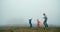Cheerful family dance on mountain meadow in fog father with kids on vacation
