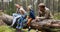 cheerful family with kids sitting and resting on fallen tree trunk after walk in forest. outdoor activities, nature adventure