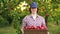 Cheerful farm worker with box of red apples in orchard