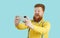 Cheerful fat man on light blue background makes selfie shot on front camera of mobile phone.