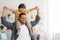 Cheerful father riding his little son on shoulders, having fun together at home, both smiling to camera, empty space