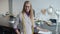 Cheerful female dressmaker standing indoors in studio near work table smiling