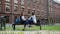 Cheerful female students chatting while sitting on bench in campus park before lessons. University friends