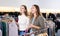 Cheerful females holding warm jumpers and sweaters on hangers while spending time together in a clothing store