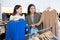 Cheerful females holding warm jumpers and sweaters on hangers while spending time together in a clothing store