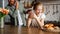 Cheerful freckled girl holding juice near sweet buns and blurred busy father working in kitchen, banner image