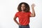 Cheerful, friendly african american woman with afro hairstyle, raising hand and waving camera with pleasant smile as