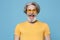 Cheerful funny elderly gray-haired mustache bearded man in casual yellow t-shirt, eyeglasses posing isolated on blue