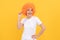 cheerful funny girl with fancy look wearing orange hair wig on yellow background, cool