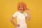 cheerful funny girl with fancy look wearing orange hair wig on yellow background, cool