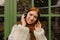 Cheerful ginger woman listening music with wireless headphones while standing outdoors