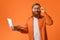 Cheerful gingerhead bearded man works on laptop on orange backdrop