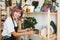 Cheerful girl with colorful hair in black apron and white T-shirt putting handmade plates on shelf happily looking in