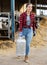 Cheerful girl dairy farm worker carrying can of milk in cowshed