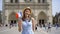 Cheerful girl enjoying vacation. Tourist in hat standing near Notre Dame of Paris. Waving French flag