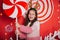A cheerful girl with horns holds a candy in her hands. A wall of lollipops. Child stands against the background of New Year`s