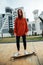 Cheerful girl in the orange hoodie rides on street on a longboard