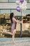 Cheerful girl with purple dress holding balloons and raising her leg