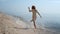 Cheerful girl running ocean waves back view. Playful woman walking wet sand.